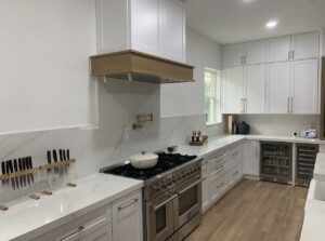 Modern kitchen with white cabinetry, marble countertops, a stainless steel stove, knife set, pot filler faucet, and built-in wine cooler. A pot is on the stove, and a small window is visible.